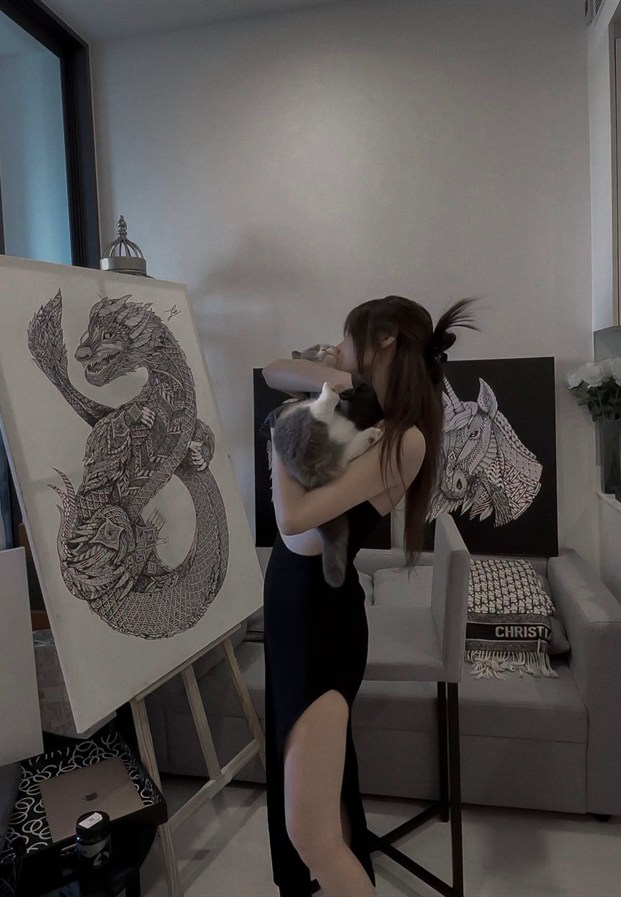 Pimnara อุ้มแมวยืนข้างผลงานภาพวาดของตัวเอง